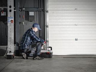 Garage Door Maintenance Service – Treasure Island Technician kneeling in front of a closed white garage door with a toolbox, performing a maintenance inspection in a Treasure Island garage.