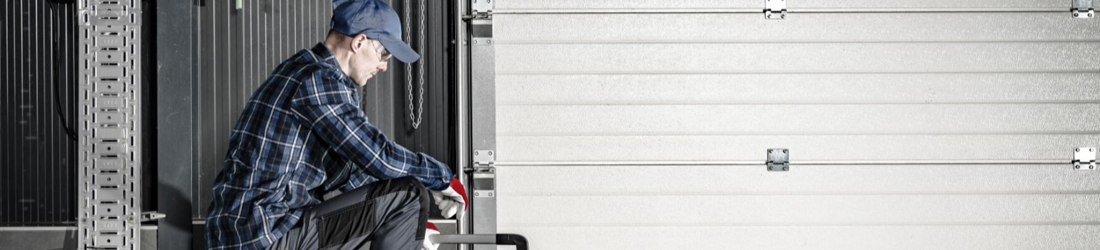Technician kneeling in front of a closed white garage door with a toolbox, performing a maintenance inspection in a Treasure Island garage.