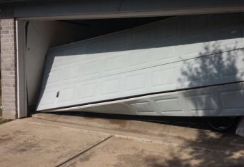 White double garage door severely off track and stuck halfway open in a brick garage in Saint Pete Beach, showing need for urgent repair.