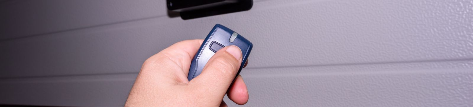 Close-up of a hand using a remote clicker to open a garage door, illustrating garage door remote clicker service in Treasure Island.