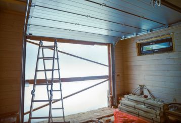 Partially installed garage door with an aluminum frame, construction ladder, and stacked building materials inside a wooden garage, showing a professional garage door replacement underway in Treasure Island.