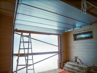 Garage Door Replacement in Progress – Professional Service in Treasure Island Partially installed garage door with an aluminum frame, construction ladder, and stacked building materials inside a wooden garage, showing a professional garage door replacement underway in Treasure Island.