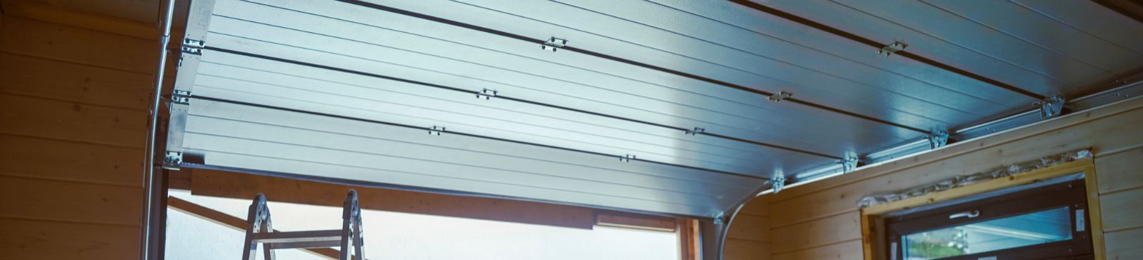 Partially installed garage door with an aluminum frame, construction ladder, and stacked building materials inside a wooden garage, showing a professional garage door replacement underway in Treasure Island.