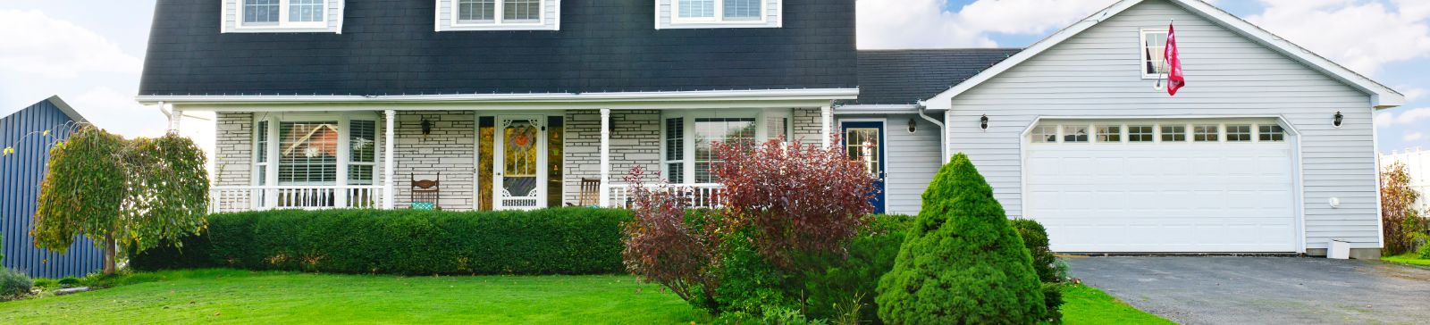 Front view of a suburban home with a large white garage door, manicured lawn, and covered porch.