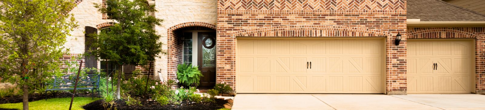 Front view of a brick house with double beige garage doors and a landscaped entryway.
