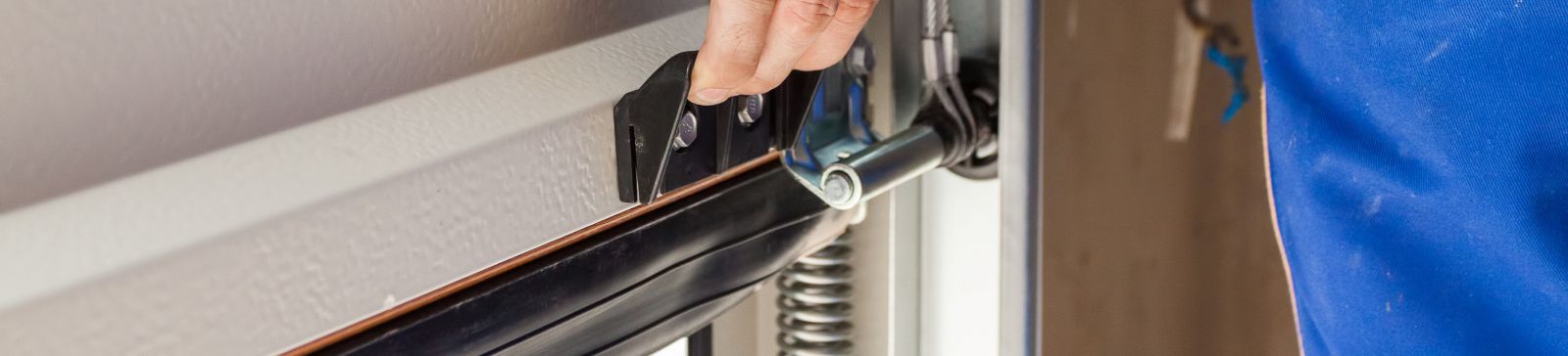 Close-up of a technician’s hand adjusting hardware on a residential garage door track, illustrating professional garage door repair and installation work in Treasure Island.