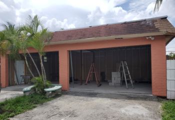 Front view of a Treasure Island home with the old garage doors removed, showing the open garage bays and preparation for new double door installation.