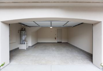 Interior view of a modern, empty garage with an open overhead garage door and visible automatic opener, illustrating innovative garage door technologies