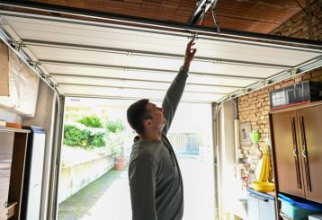 Man inside a residential garage reaching up to manually open a garage door, illustrating common problems when a garage door won’t open or close.